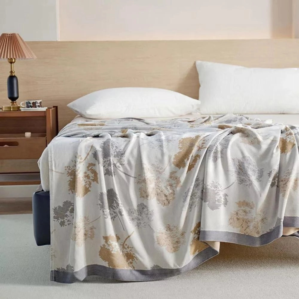 Luxury floral silk comforter draped over a bed in a stylishly decorated bedroom, featuring grey tones, wooden furniture, and cabinets, showcasing elegant interior design with a focus on comfort and high-quality textile.