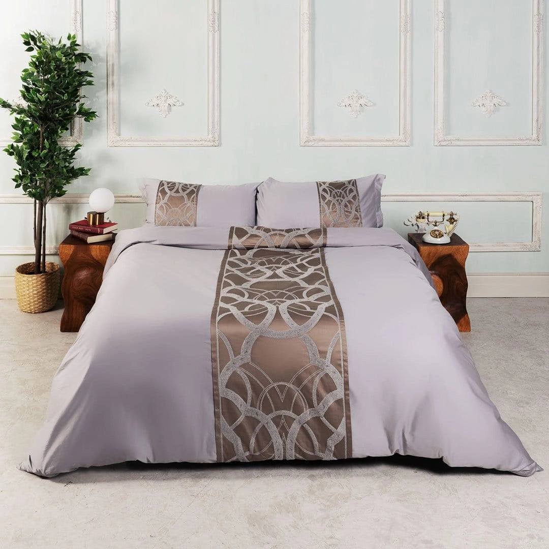 Luxury geometric satin bedding set in taupe gray on a California King bed, featuring a stylish comforter with a geometric pattern. The room includes elegant interior design elements such as a wooden bed frame and hardwood flooring. A houseplant adds a touch of greenery and comfort.