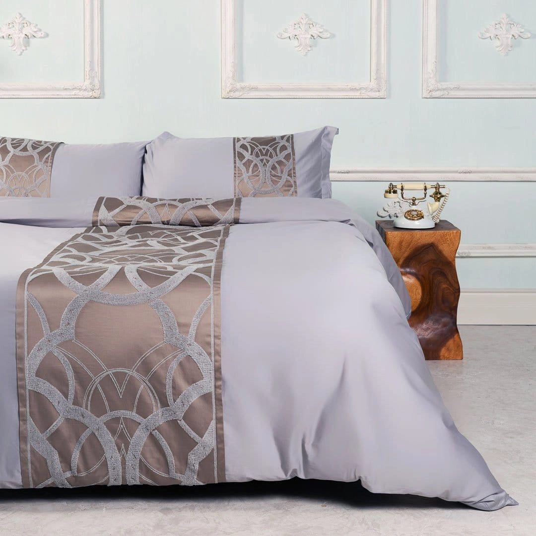 Luxury geometric satin bedding set in taupe gray on a well-made bed, featuring a modern and elegant design, surrounded by stylish interior decor elements including wooden flooring and complementary furnishings.