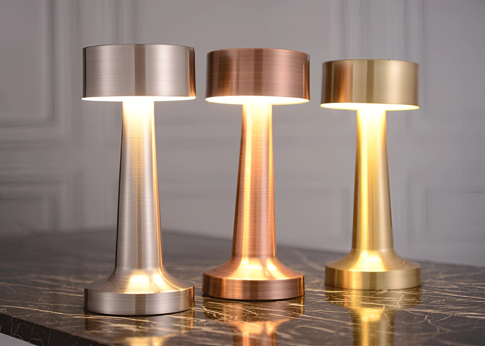 A luxury cordless LED table lamp featuring a gold finish, designed in a cylindrical shape and placed on a wooden table, providing soft ambient light.