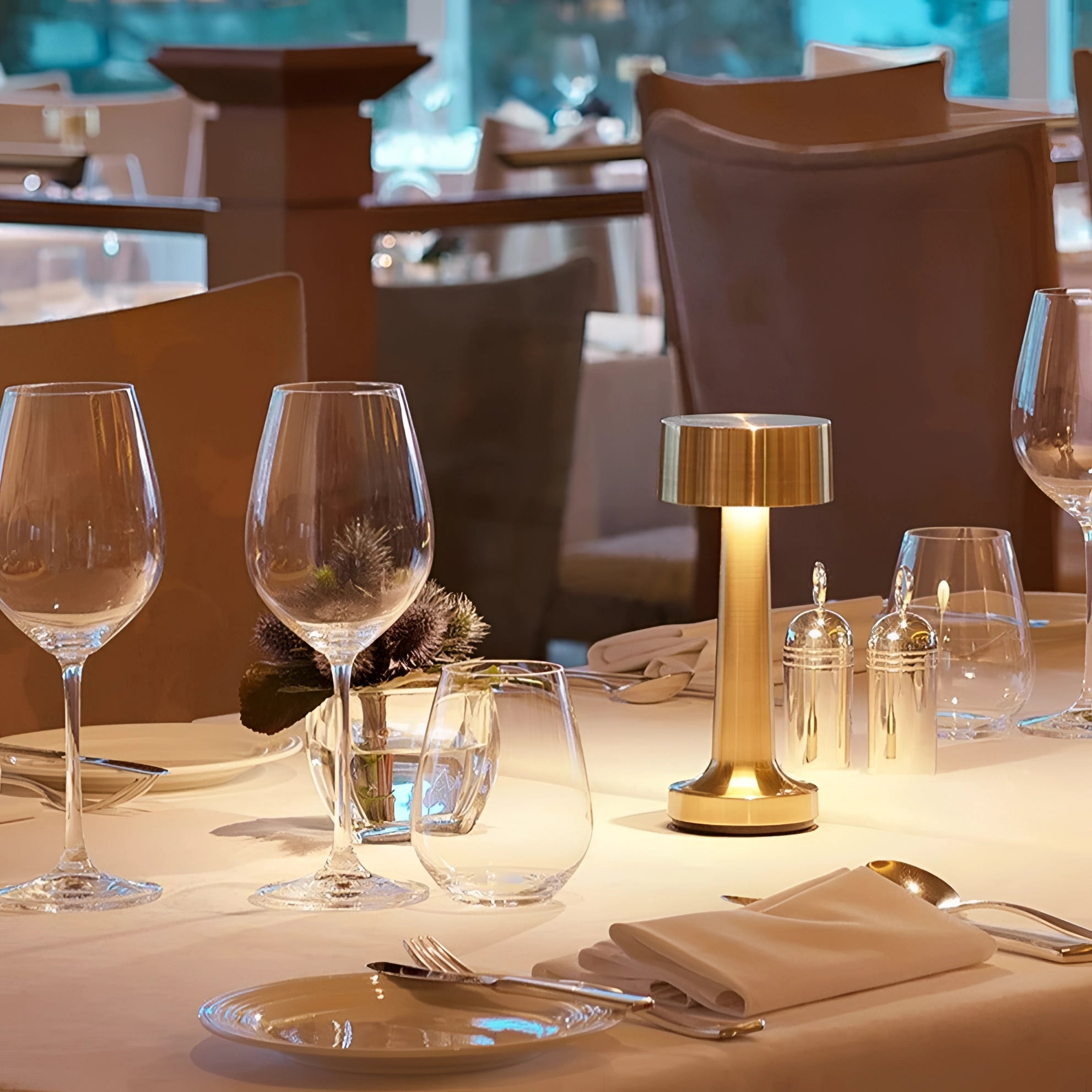 A stylish luxury gold cordless LED table lamp elegantly placed on a table setting, surrounded by stemware and drinkware, creating a sophisticated ambiance.
