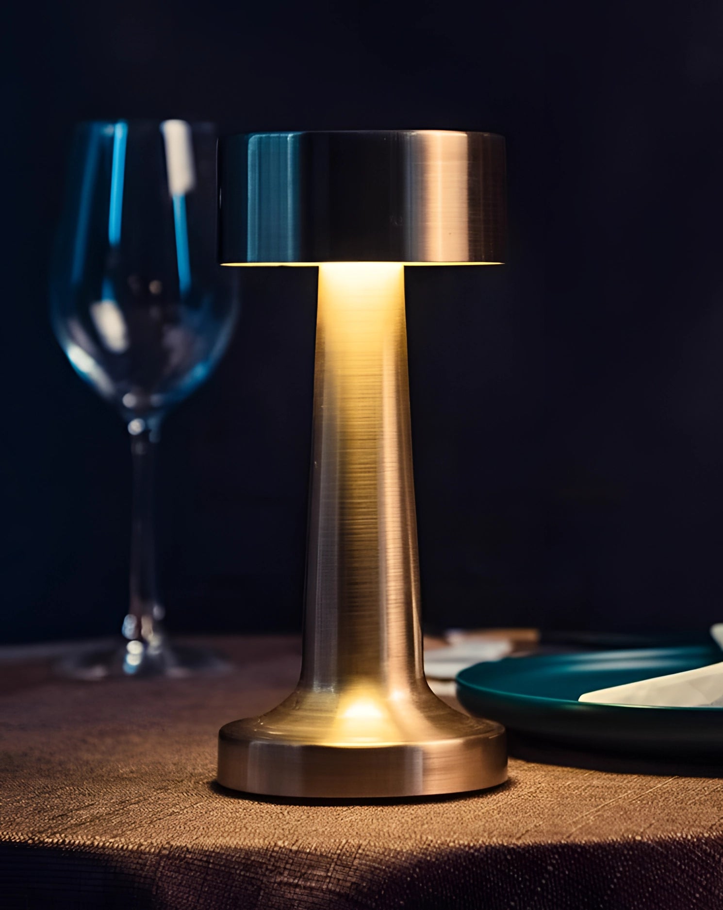 A luxury gold cordless LED table lamp with a sleek, portable design, illuminating a table setting with elegant glassware and wine glasses, creating a sophisticated ambiance.