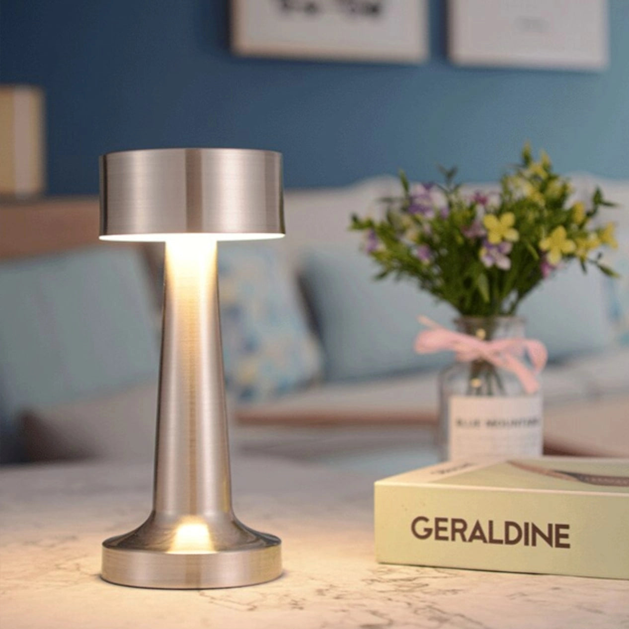 Luxury gold cordless table lamp on a wooden table with an elegant design, accompanied by a vase of flowers, enhancing the interior decor.