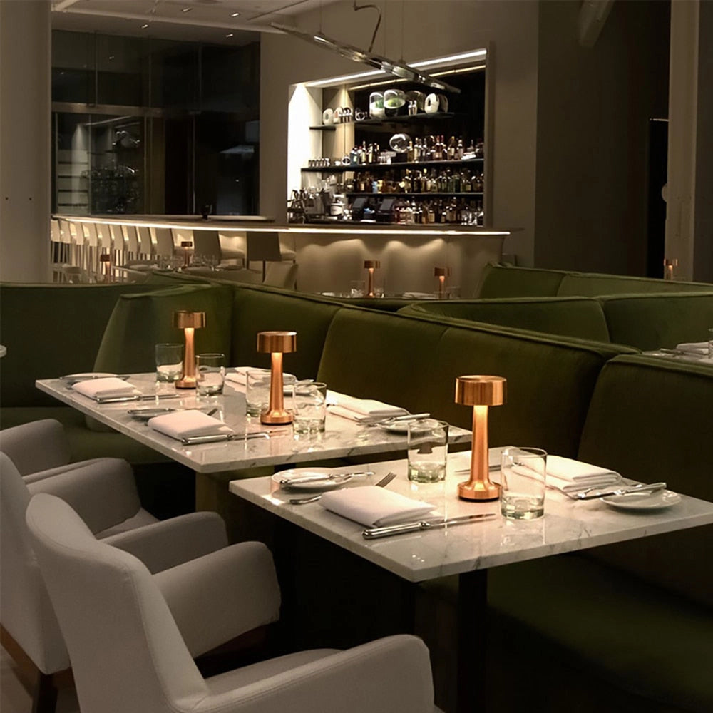 Luxury gold cordless table lamp on a dining table with elegant tableware and chairs in a well-designed interior.