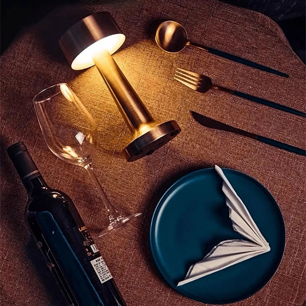 Elegant dining table setup featuring luxury gold cordless rechargeable table lamp, surrounded by tableware including plates, cutlery, and drinkware.