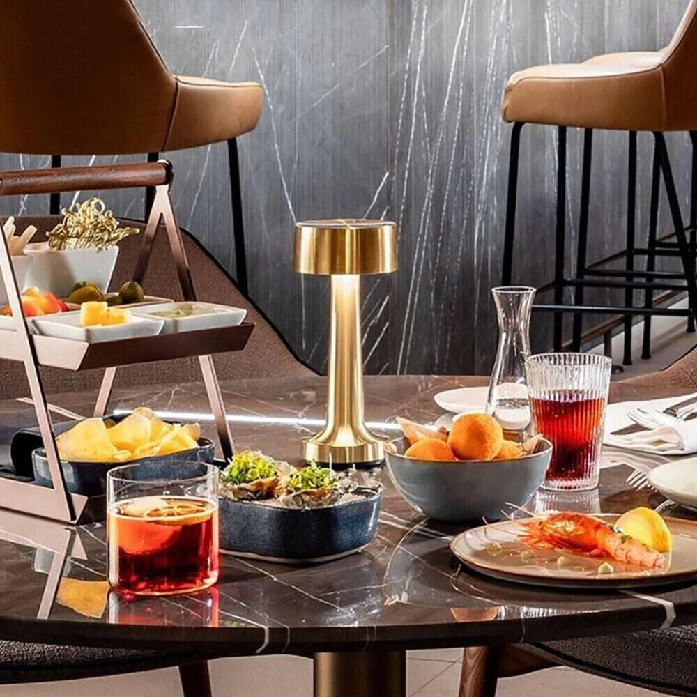 Luxury gold cordless table lamp on an elegantly set dining table with dishware, tableware, and plates, enhancing the interior design.