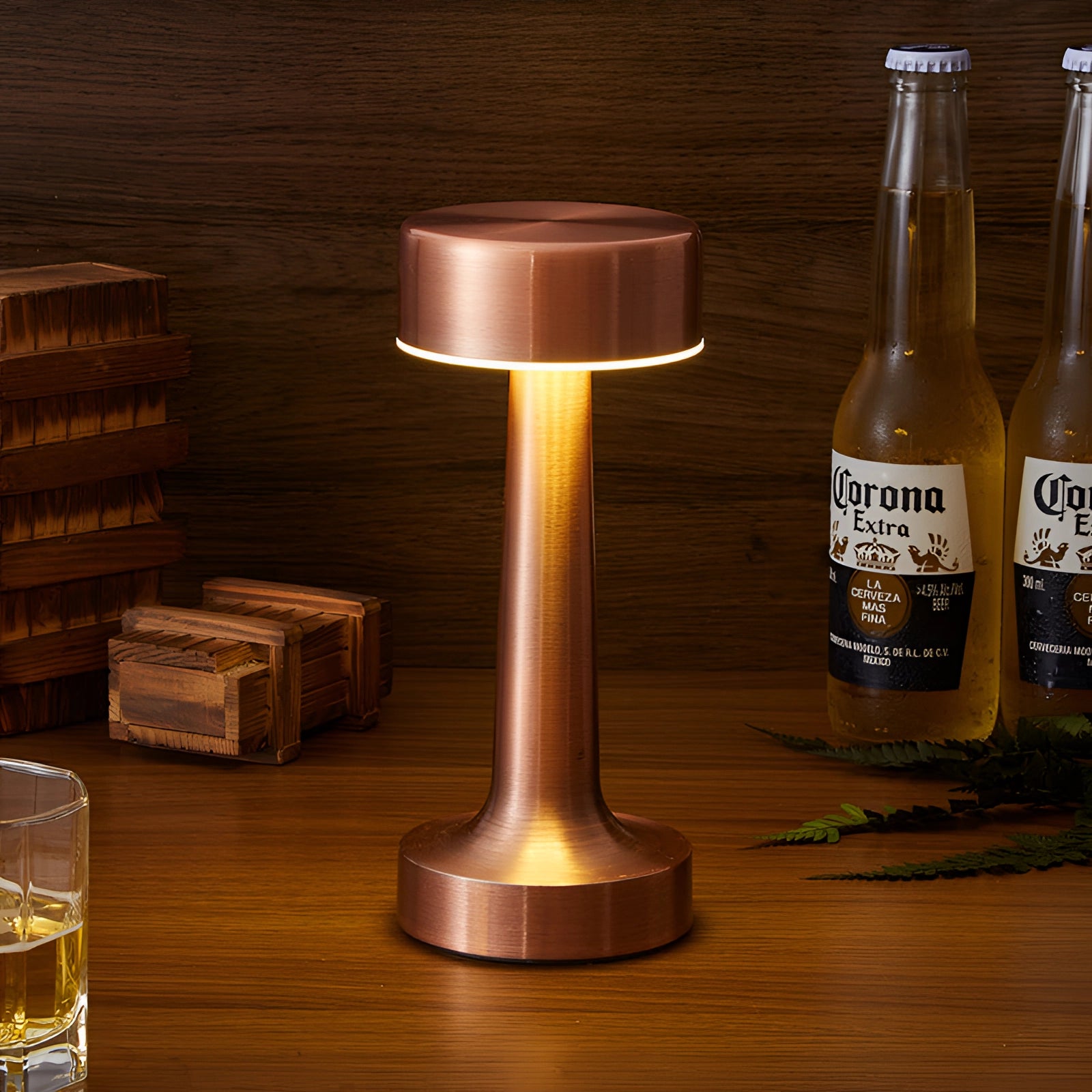 A luxury gold cordless table lamp sits elegantly on a wooden table, surrounded by various drinkware including bottles and glasses, creating a sophisticated dining ambiance.