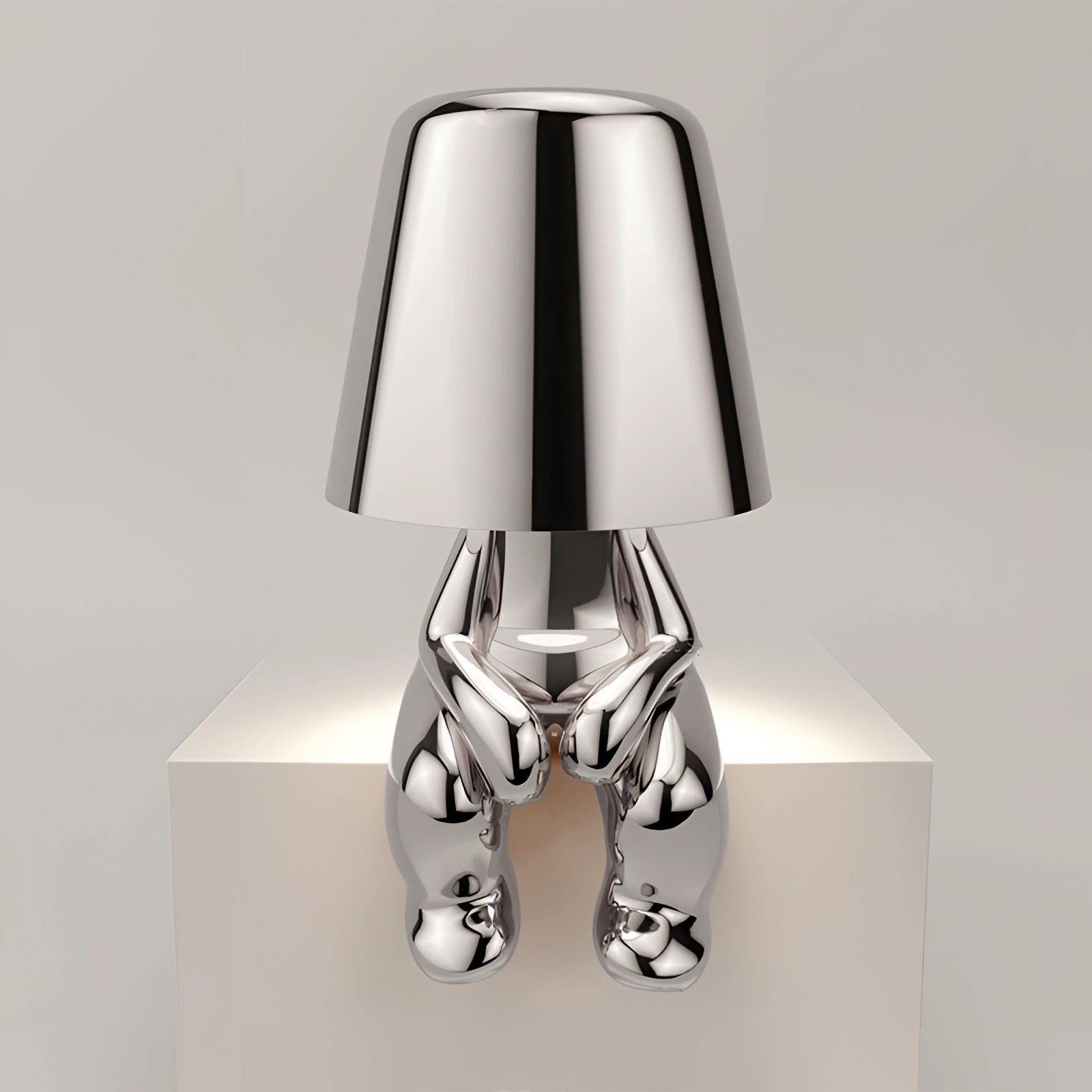 Luxury metallic gold table lamp with a modern sculptural design, featuring a silver variant finish. The lamp has a rectangular shape with a metal base and a fabric lampshade, combining artistic elements with functional lighting.