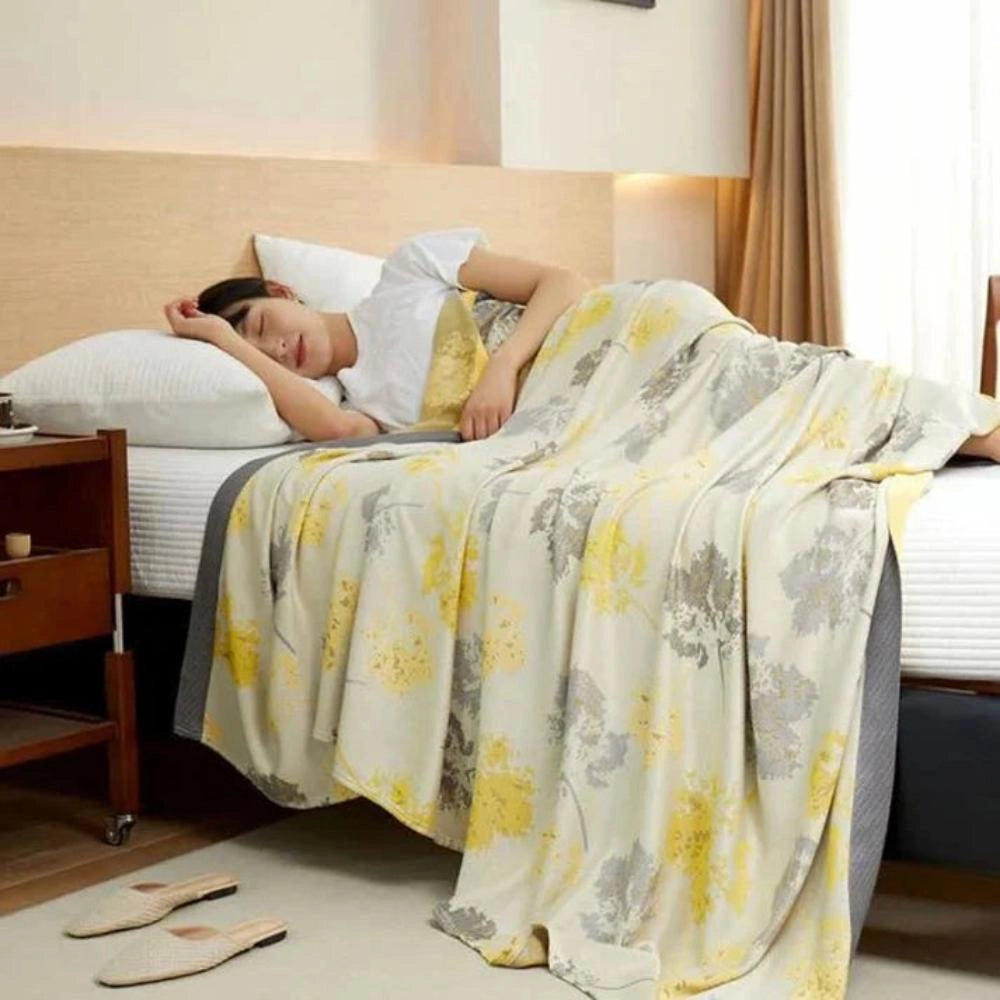 Luxury silk floral throw blanket draped over a bed with a wooden bed frame, surrounded by elegant home decor including a lamp and curtains, all set on hardwood flooring.