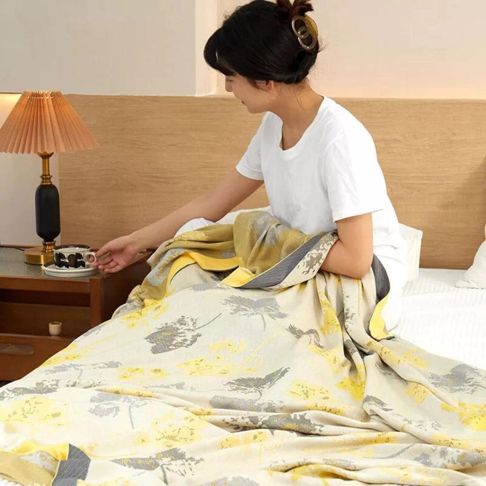 Luxury silk floral throw blanket draped elegantly over a stylish chair in a well-appointed room, showcasing its intricate floral pattern and luxurious texture, complemented by a warm and inviting ambiance.