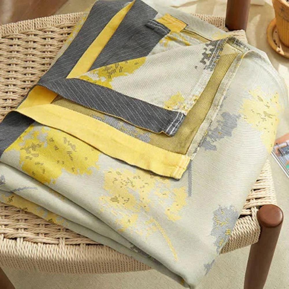 Luxury silk floral throw blanket in shades of yellow and beige, elegantly draped over a wooden surface, showcasing its intricate pattern and designer appeal.