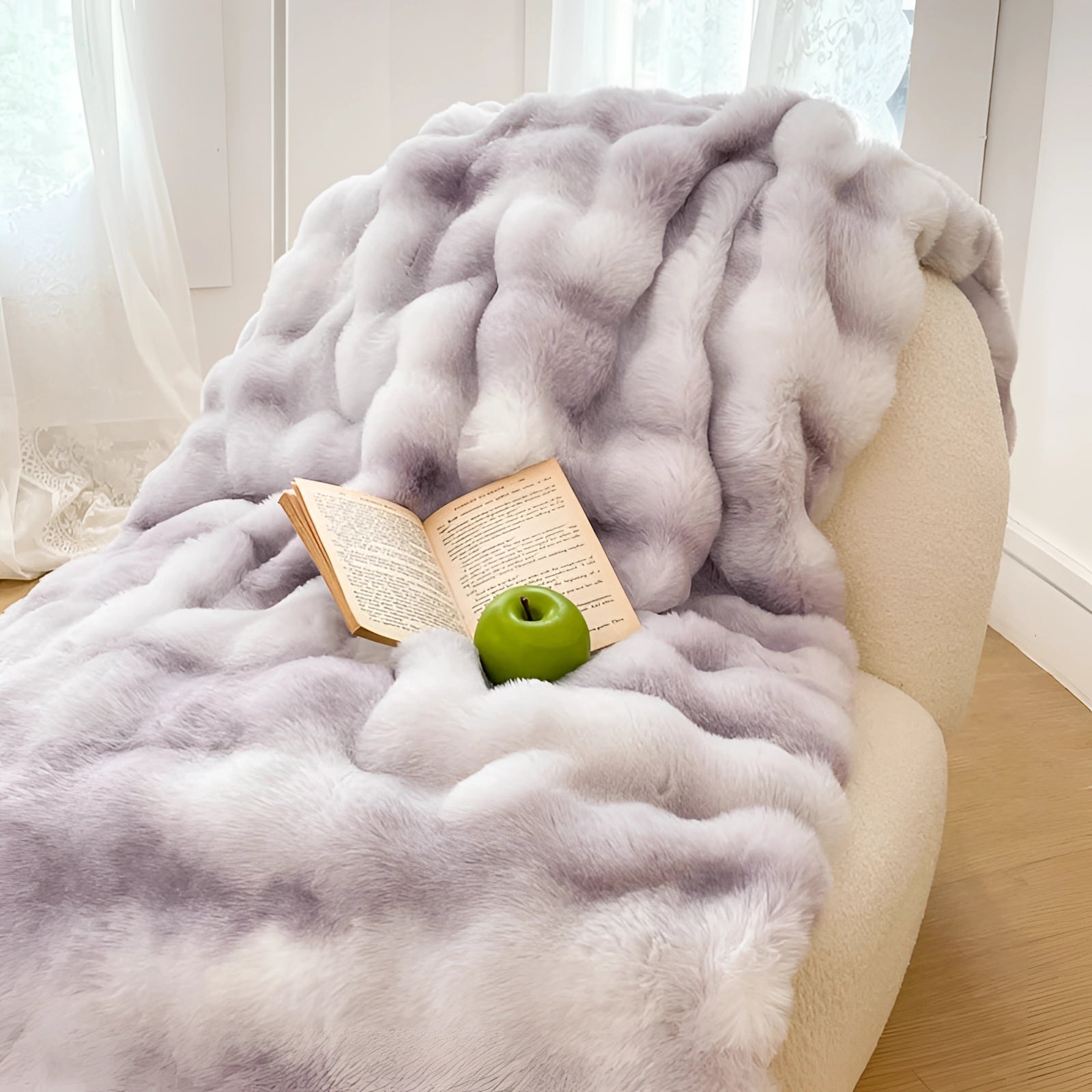Luxury white faux fur accent chair with plush texture, featuring a light gray color and dimensions of 200cm x 230cm. The chair is elegantly designed for comfort, ideal for a cozy reading nook, and is complemented by soft throw pillows. The setting suggests a sophisticated interior design with an emphasis on comfort and style.