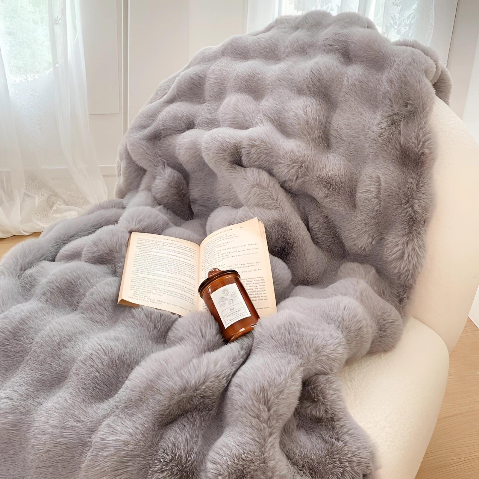 Luxury white faux fur accent chair with plush texture, styled in a cozy reading nook setting. A person's hand is visible, gently touching the chair, showcasing comfort and softness. The surrounding ambiance includes a dark gray linen throw, enhancing the inviting atmosphere.
