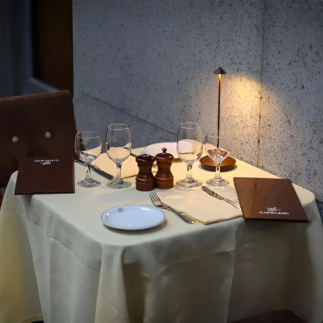 Minimalist arrow-shaped LED desk lamp on a modern dining table with elegant tableware and serveware, set in a contemporary interior design setting.