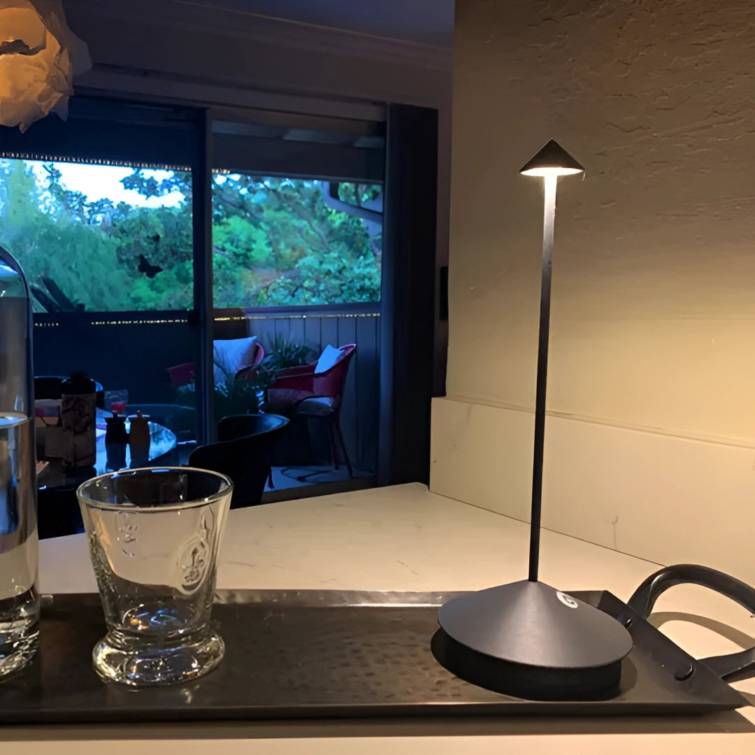 Minimalist arrow-shaped LED desk lamp with a sleek design, ideal for modern interior decor, positioned on a table with surrounding tableware and drinkware elements.