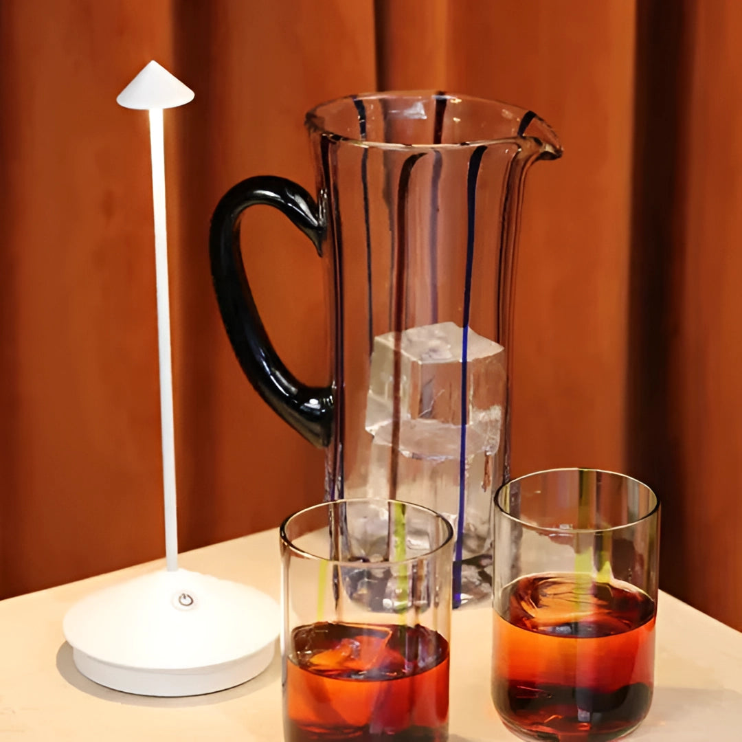 A minimalist arrow-shaped LED desk lamp with a sleek modern design, positioned on a table beside various tableware items, including a cup and dishware, complementing the contemporary decor.