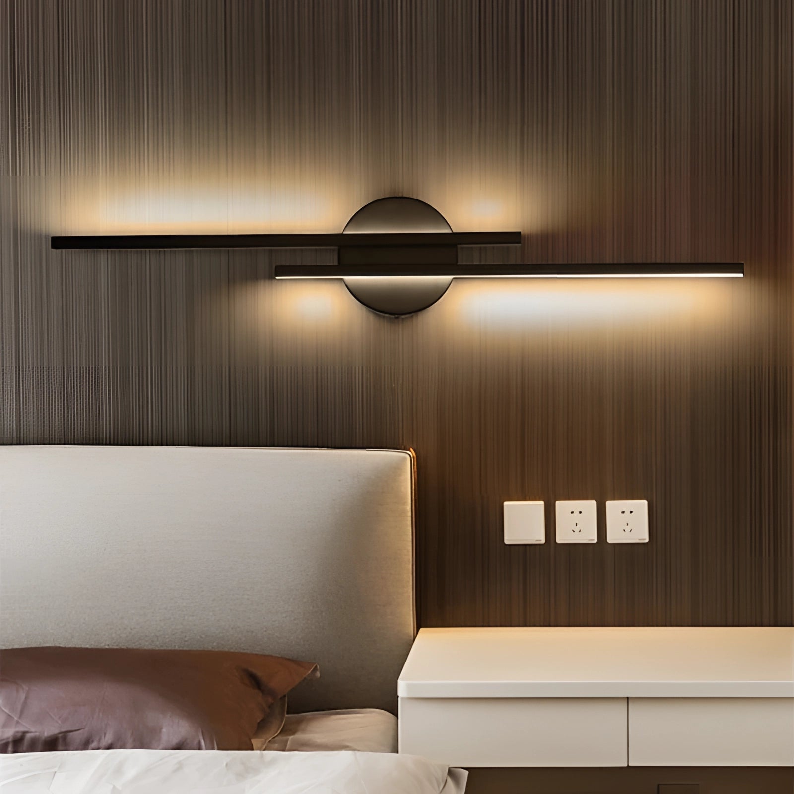 Minimalist black LED wall sconce in a modern vertical metal design, emitting cold light, mounted on a wall above a brown couch in a stylishly furnished living room with wooden accents.