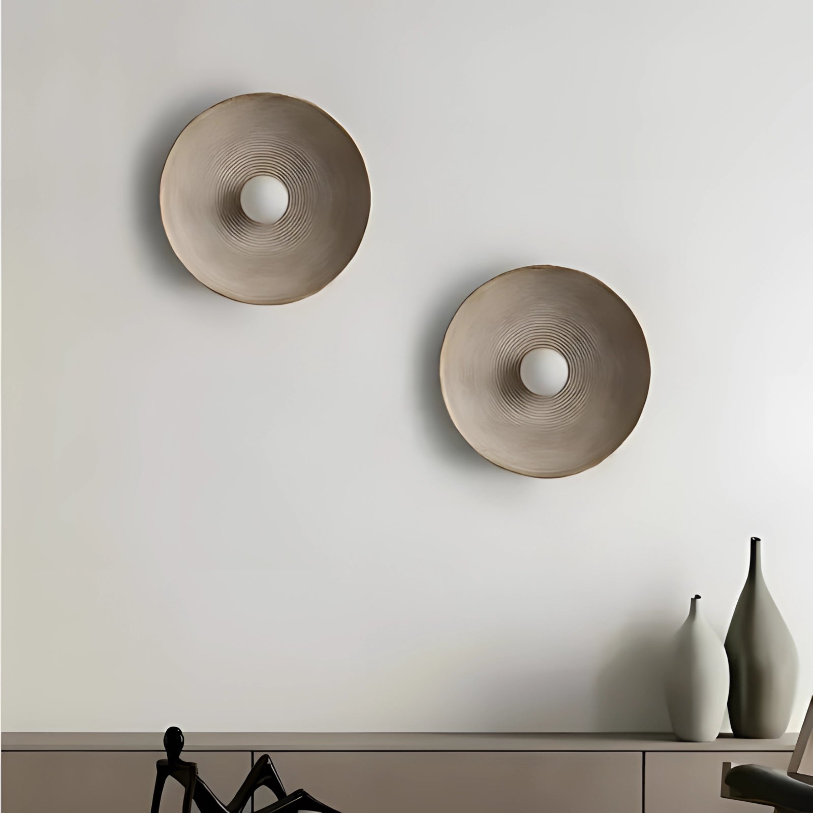 Minimalist bronze circular wall art sculpture with a metallic finish, featuring a sleek design that reflects light, creating a sophisticated aesthetic against a grey background.
