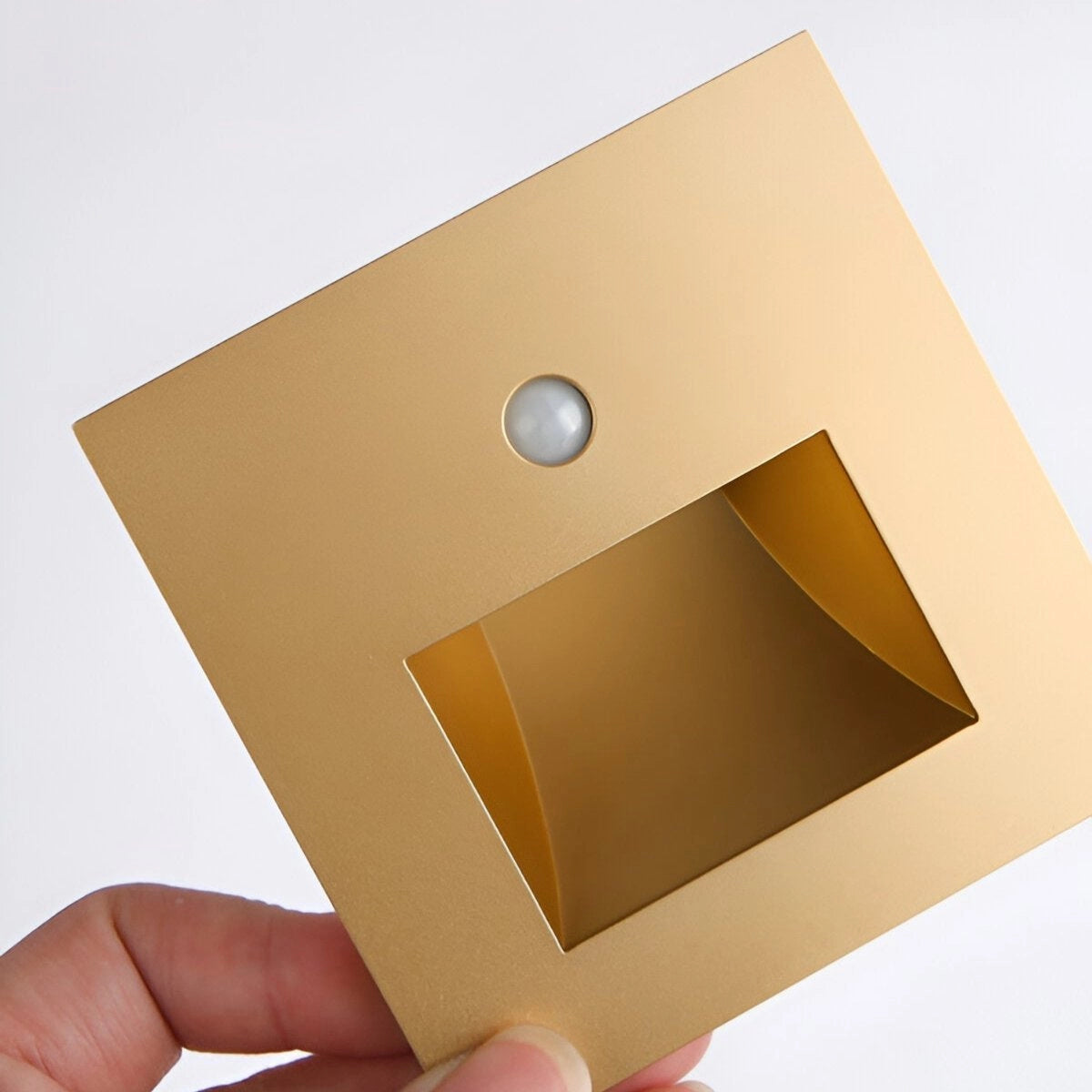 Minimalist child-safety light switch cover in beige and gold tones with a rectangular shape, designed to be anti-shock and measuring 86x86mm, displayed on a wooden surface.