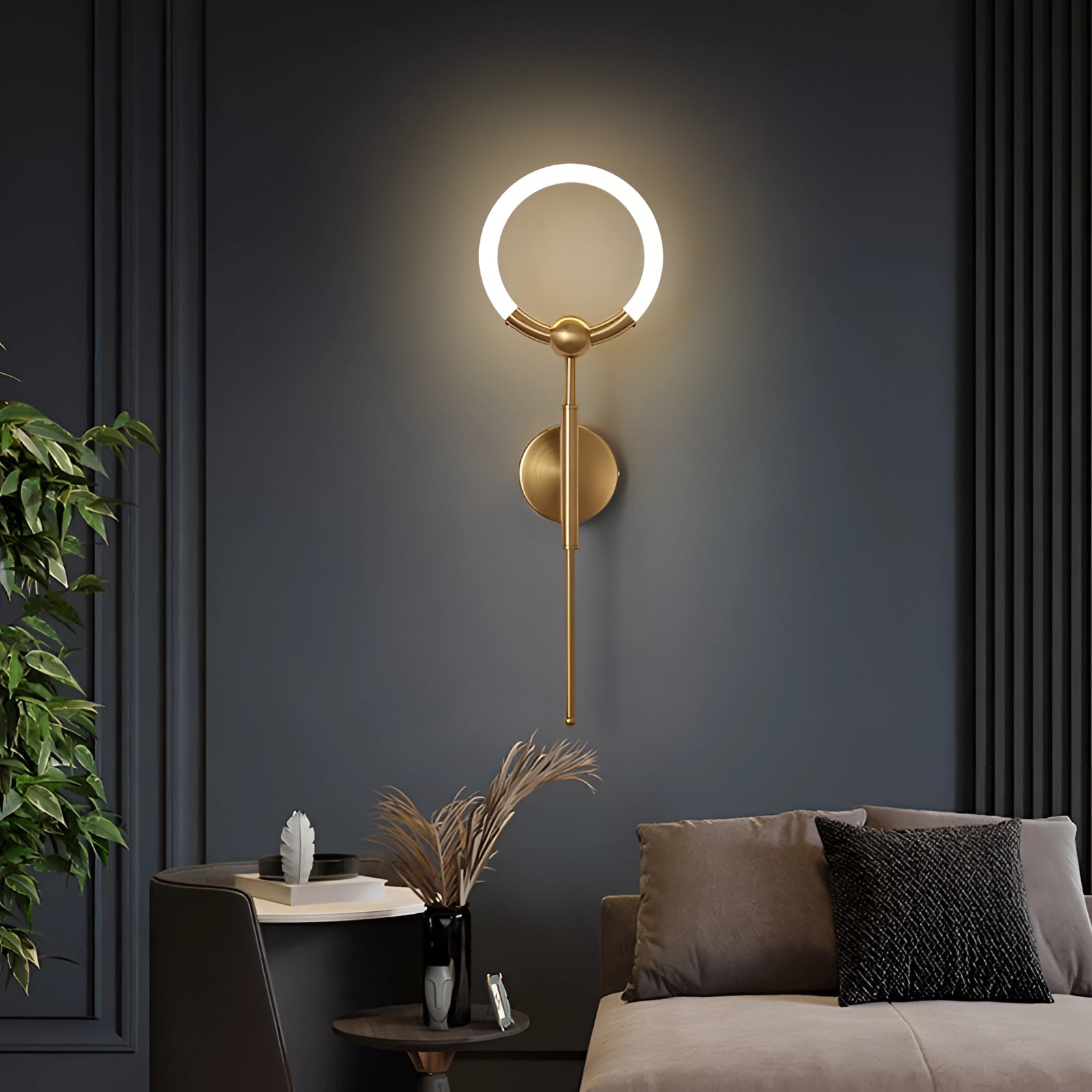 Minimalist circular LED wall lamp in gold, featuring a modern sconce design, mounted on a wall in a contemporary interior setting with wooden elements and decorative plants.