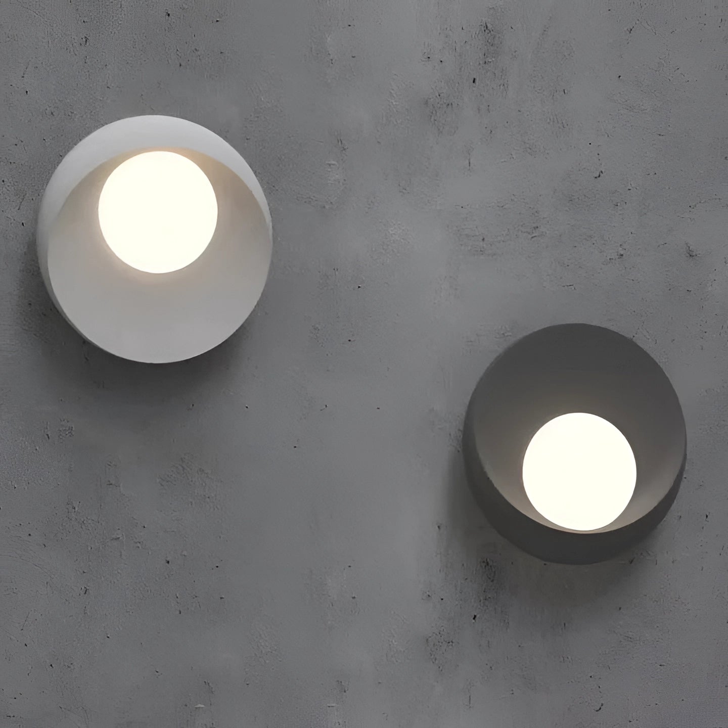 Minimalist eye-shaped wall sconce with a modern design, featuring a sleek grey finish and circular elements, mounted on a wooden backdrop. The lighting fixture is illuminated, casting gentle tints and shades, creating an ambient atmosphere.