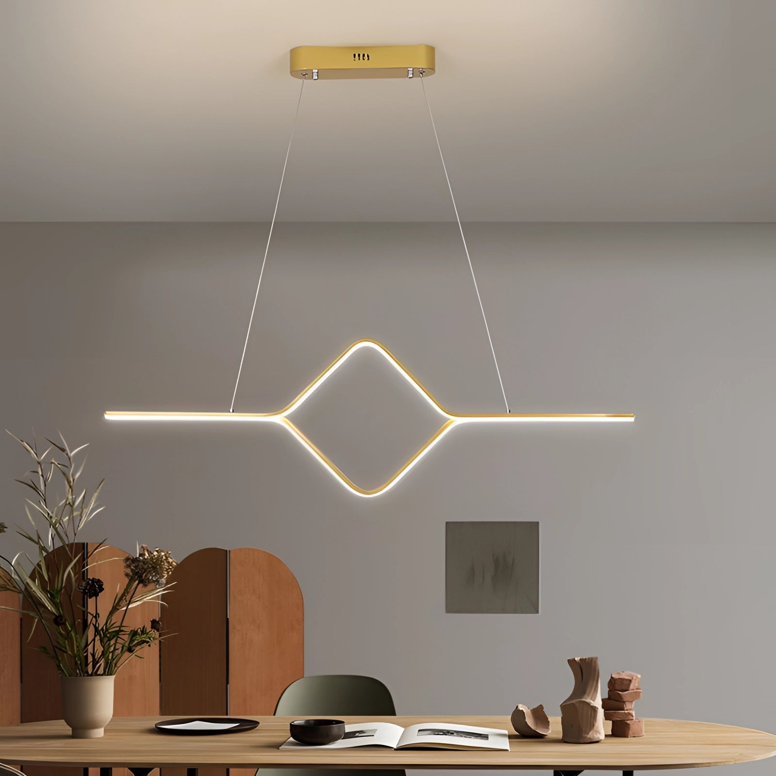 Minimalist gold LED geometric pendant light fixture hanging in a stylishly designed interior space near a window, with houseplants and a table below, casting a warm white glow.