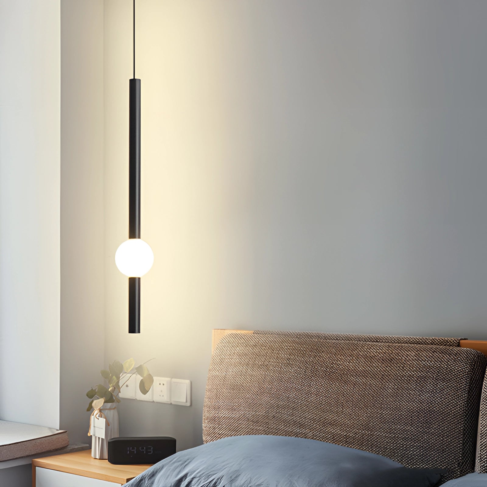 Minimalist LED pendant light in black and white with a cylindrical globe design, hanging in a modern living room setting with wooden flooring and complementary interior design elements.