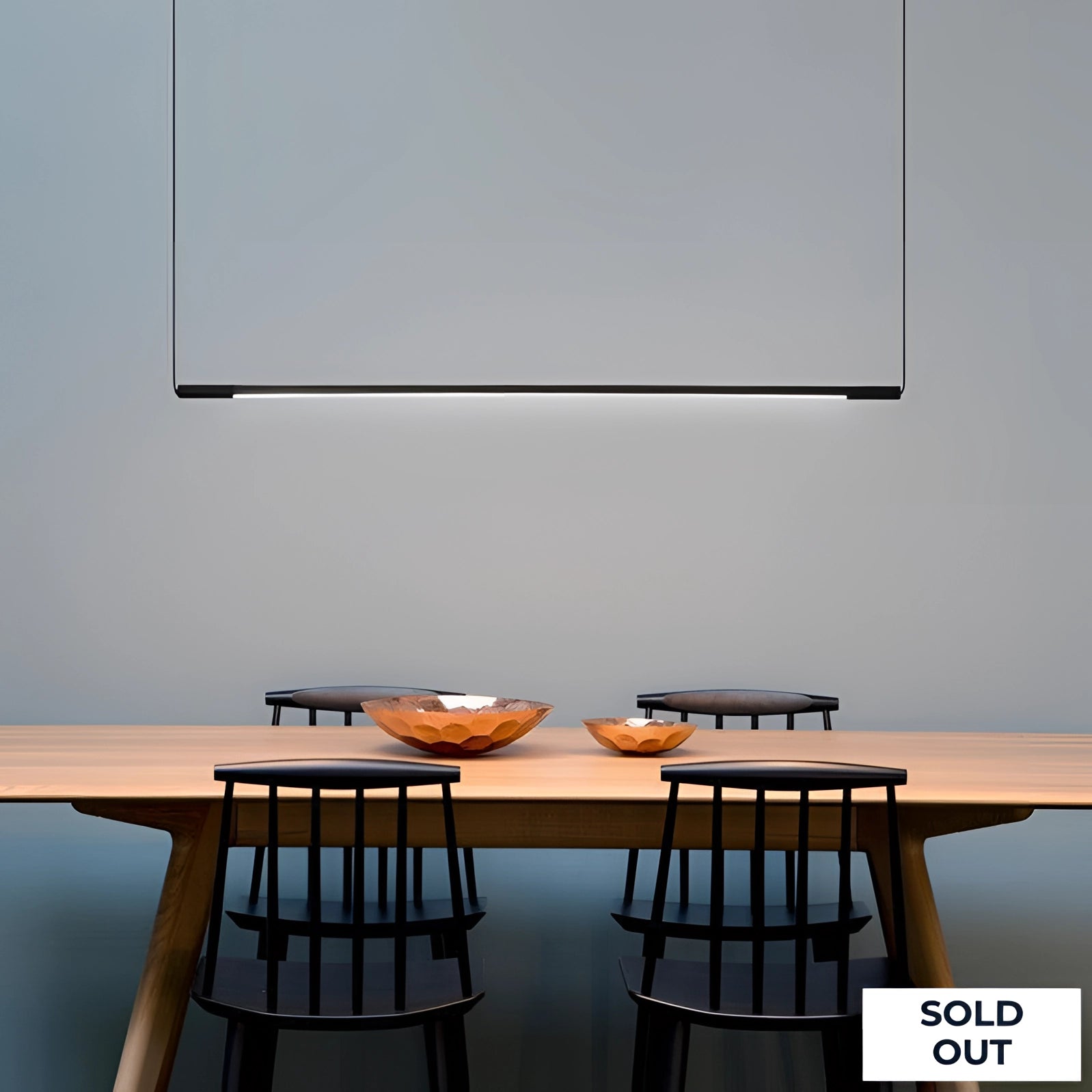 Minimalist LED pendant light hanging over a modern dining table with wooden chairs, showcasing a sleek interior design with clean lines and contemporary furniture.