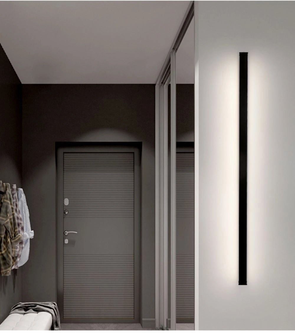Minimalist LED wall sconce mounted on a grey wall beside a wooden door, featuring a sleek modern vertical light fixture design.
