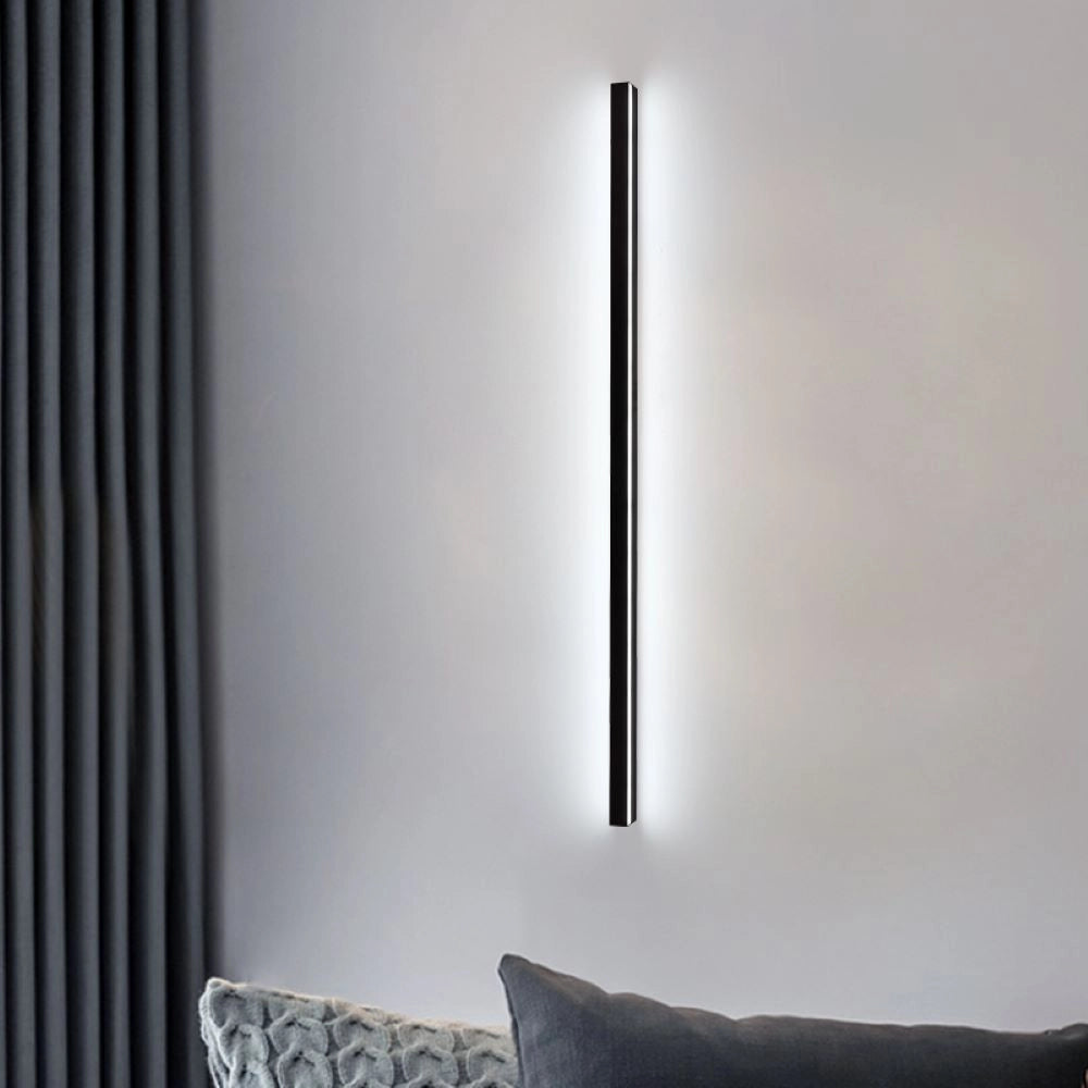 Minimalist LED wall sconce mounted on a grey living room wall above a modern couch, featuring a sleek vertical design that complements the contemporary furnishings and wooden flooring.