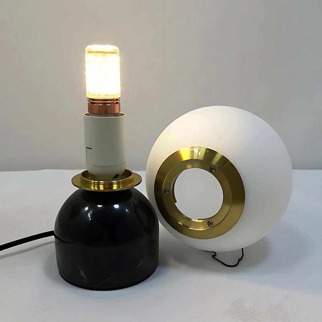 Minimalist marble table lamp with a modern orb globe design, featuring a Scandinavian aesthetic with a circular metal base and cylindrical elements.