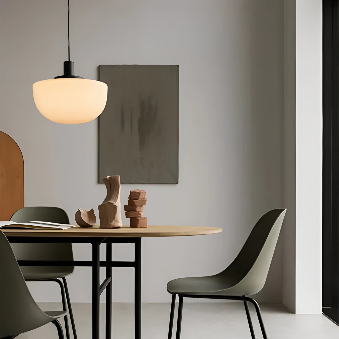 Minimalist pendant light hanging above a modern Scandinavian dining room setup, featuring a wooden table and chairs with a sleek interior design.