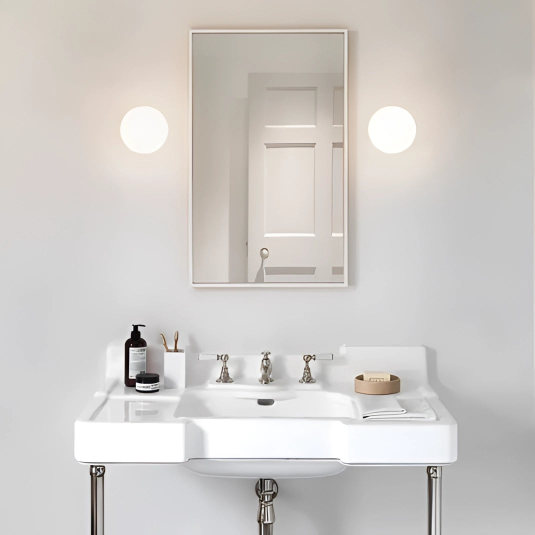 Minimalist round LED wall lights installed above a modern bathroom sink with a mirror, tap, and a sleek bathroom cabinet in a contemporary bathroom setting.