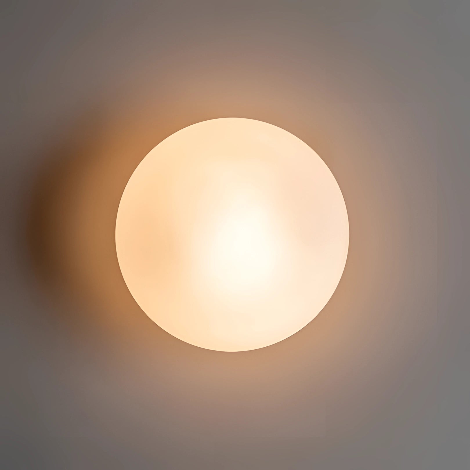 Minimalist round LED wall light with a contemporary design, emitting a soft glow reminiscent of a full moon, set against a neutral background to enhance modern bathroom aesthetics.