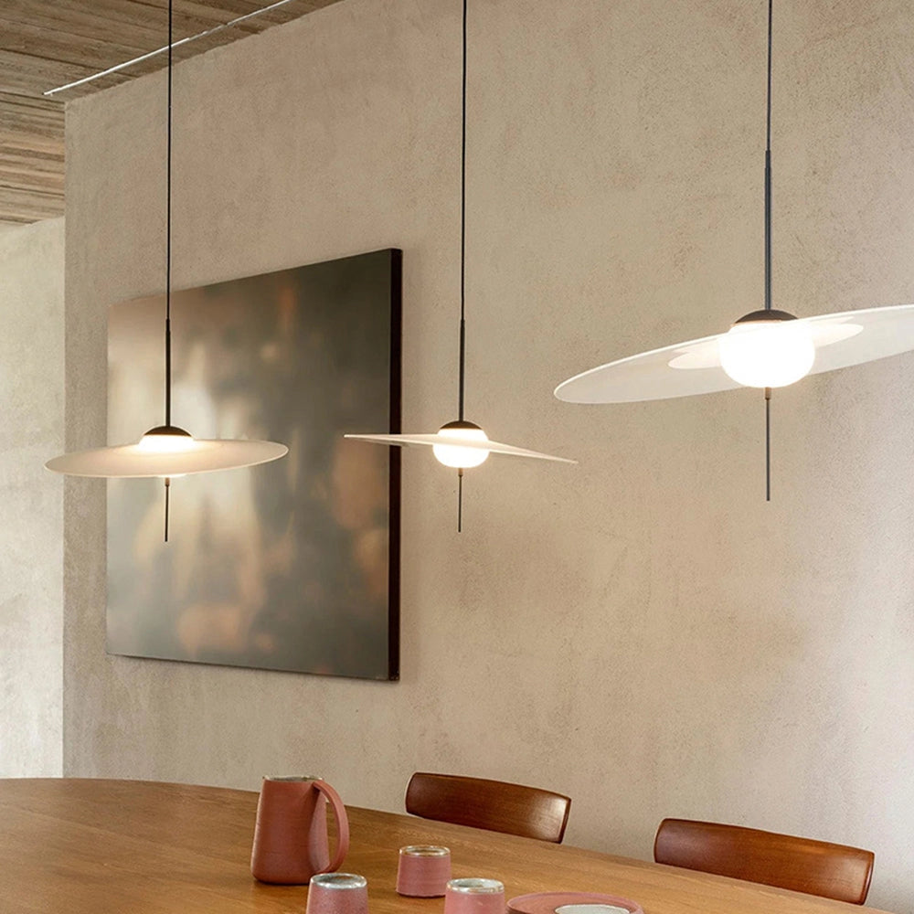 Minimalist round pendant light with an adjustable design, featuring a modern ceiling fixture, hanging above a beige interior setting with wooden flooring and table.