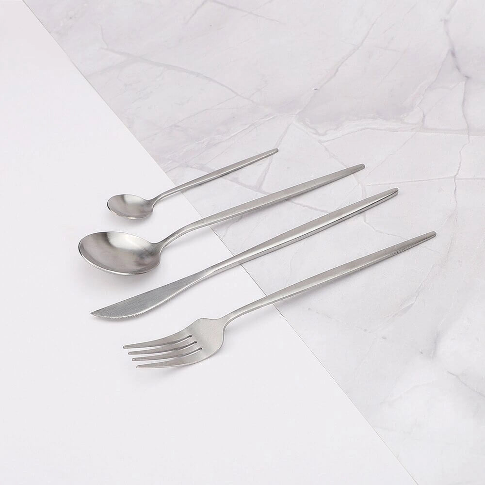 Minimalist stainless steel cutlery set displayed on a wooden table with a linen tablecloth, featuring a fork and other flatware pieces, ideal for elegant dining events.
