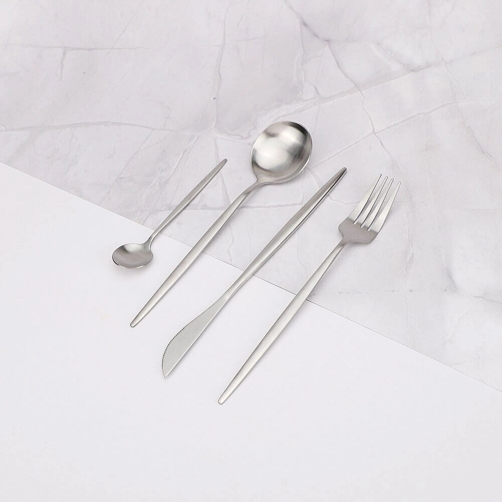 Minimalist stainless steel cutlery set featuring elegant flatware pieces arranged on a table with a circular metal plate, showcasing modern and sophisticated design.