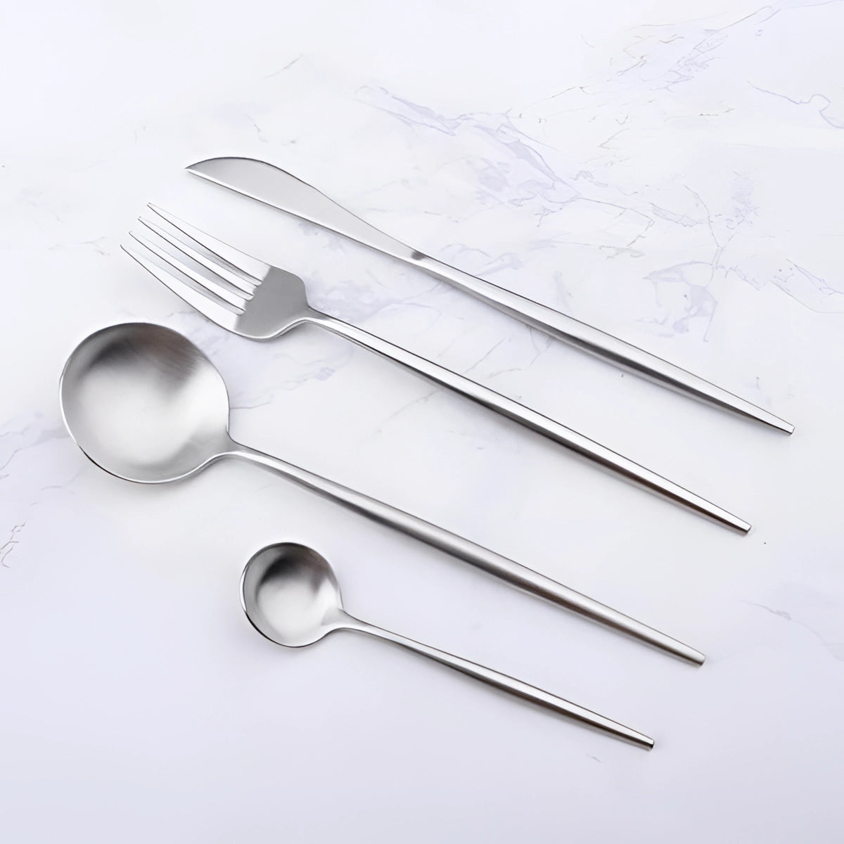 Minimalist stainless steel cutlery set featuring a modern design with sleek, elegant lines, including forks, knives, and spoons arranged on a table setting.