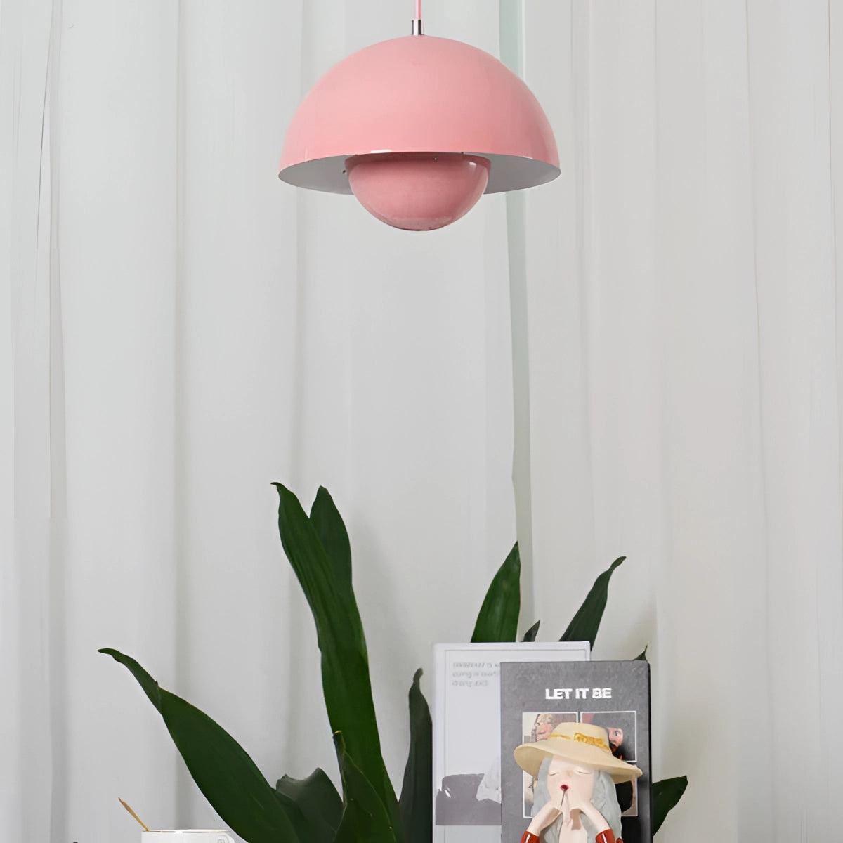 Minimalist white dome pendant light with a pink finish hanging above a dining table, surrounded by houseplants and flowers.