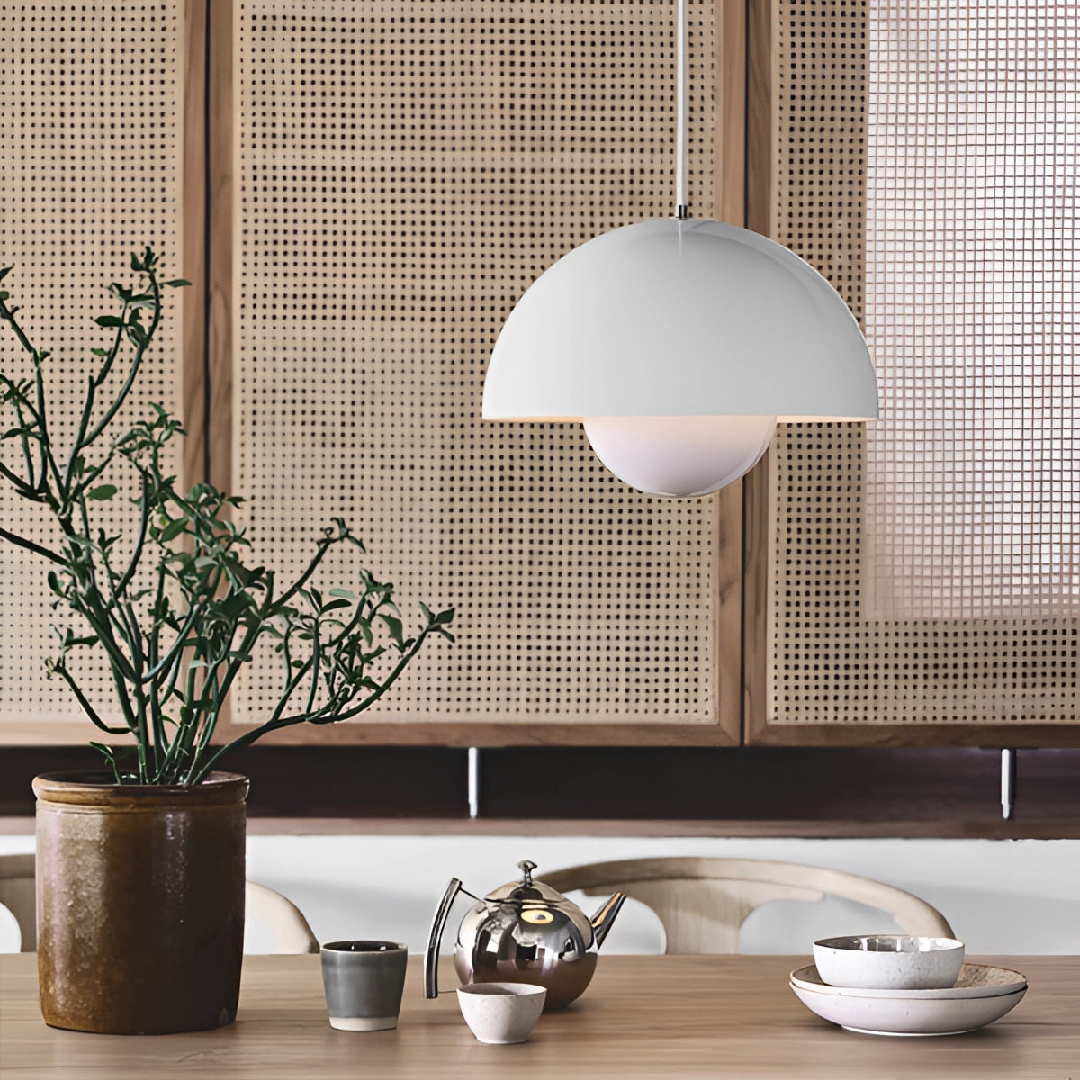 Minimalist white dome pendant light hanging above a dining table, surrounded by indoor plants and modern Scandinavian interior design elements.