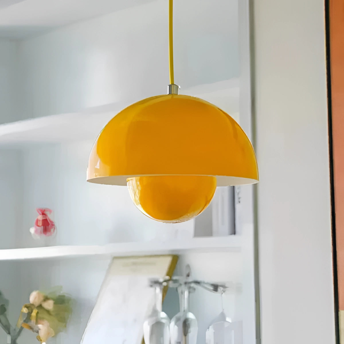 Minimalist white dome pendant light with a subtle yellow hue hanging from the ceiling, enhancing the Scandinavian style ambiance in a room with wooden shelving and natural decor elements.
