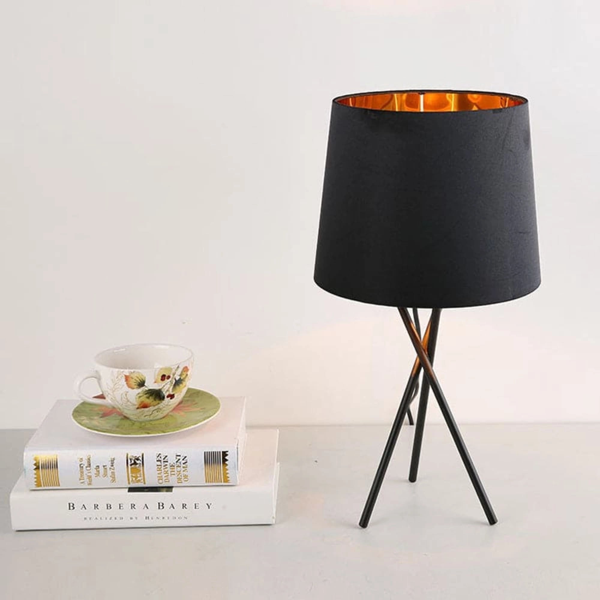 Minimalist black tripod table lamp with a modern design featuring a fabric shade, placed on a table surface.