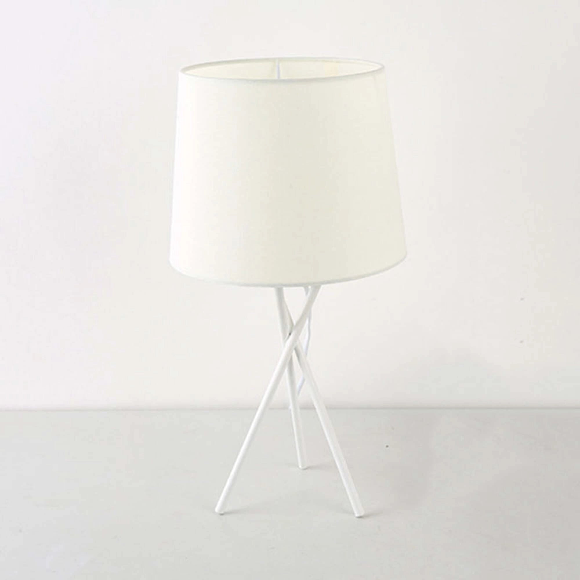Minimalist white table lamp with a modern tripod design and a fabric lampshade, featuring elements of wood and metal, positioned on a wooden table.