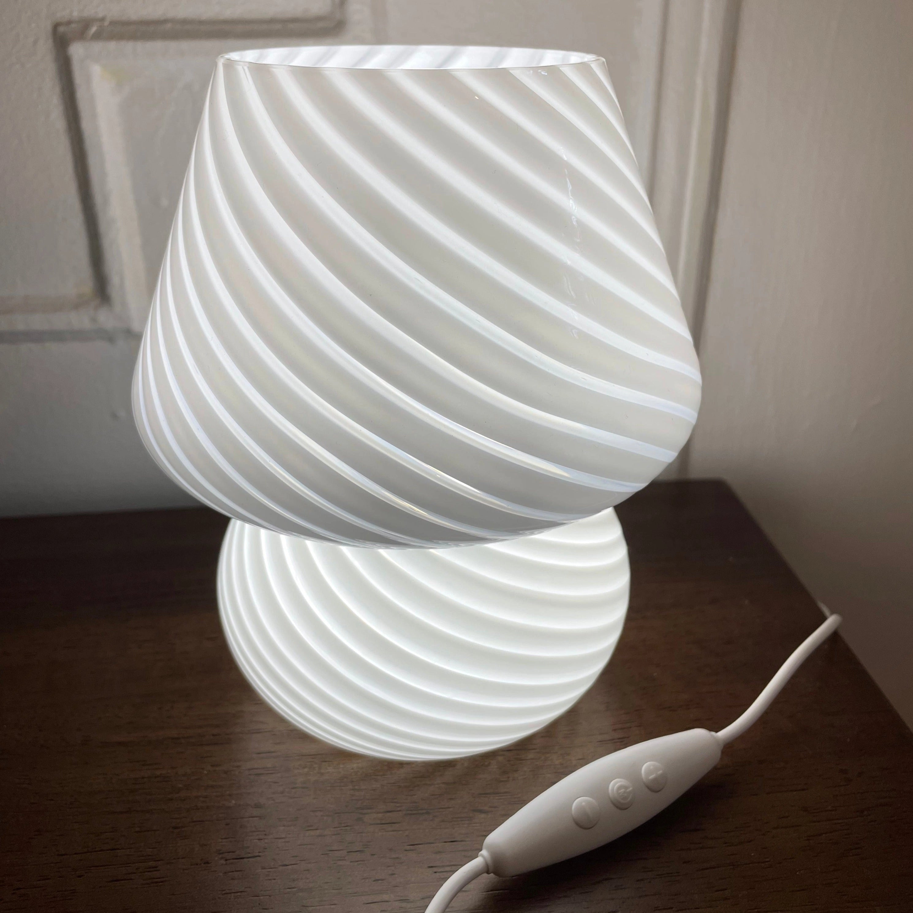 Modern 3D printed white swirl LED table lamp placed on a wooden desk.