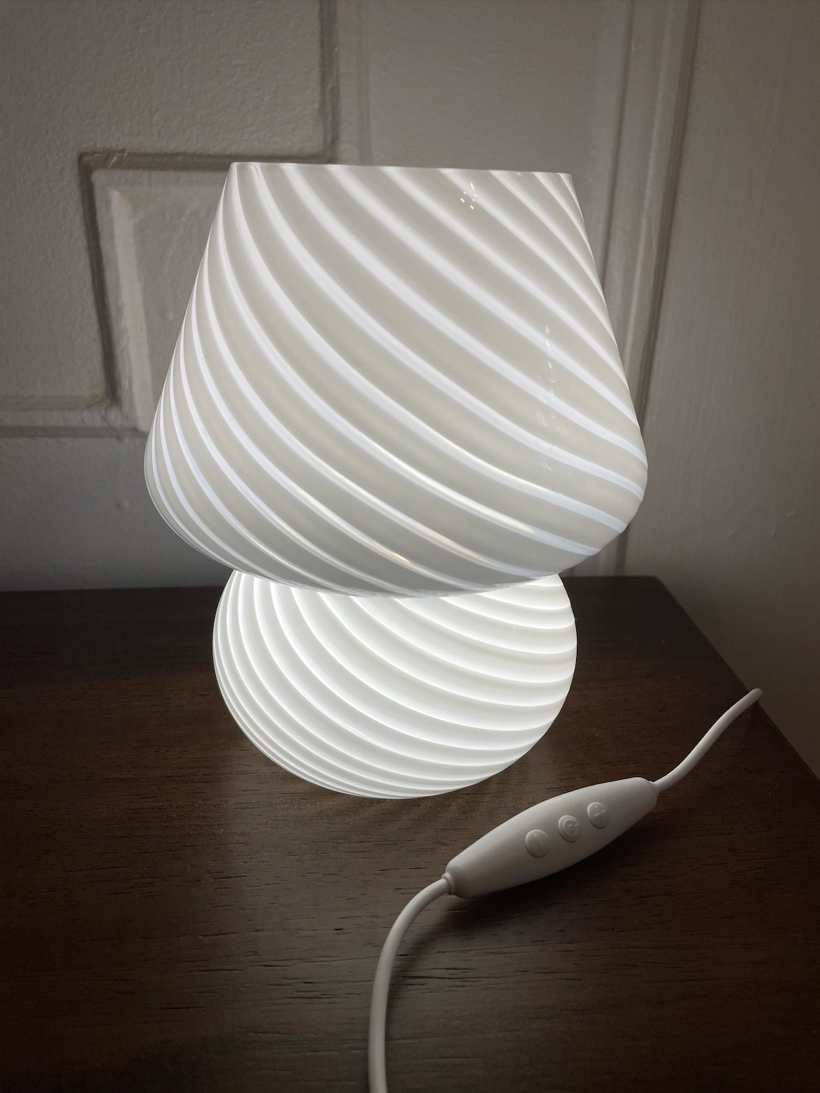Modern 3D printed white swirl LED table lamp with an energy-efficient design, featuring a unique swirl pattern and soft white lighting, placed on a wooden floor.