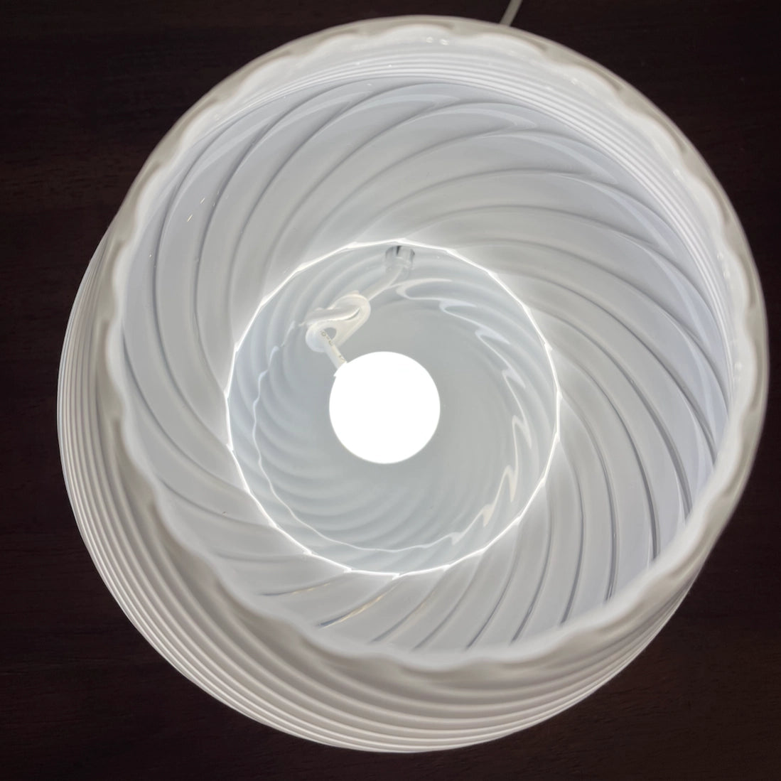Modern 3D printed white table lamp with a swirl design illuminated by LED lights, showcasing its energy-efficient features.