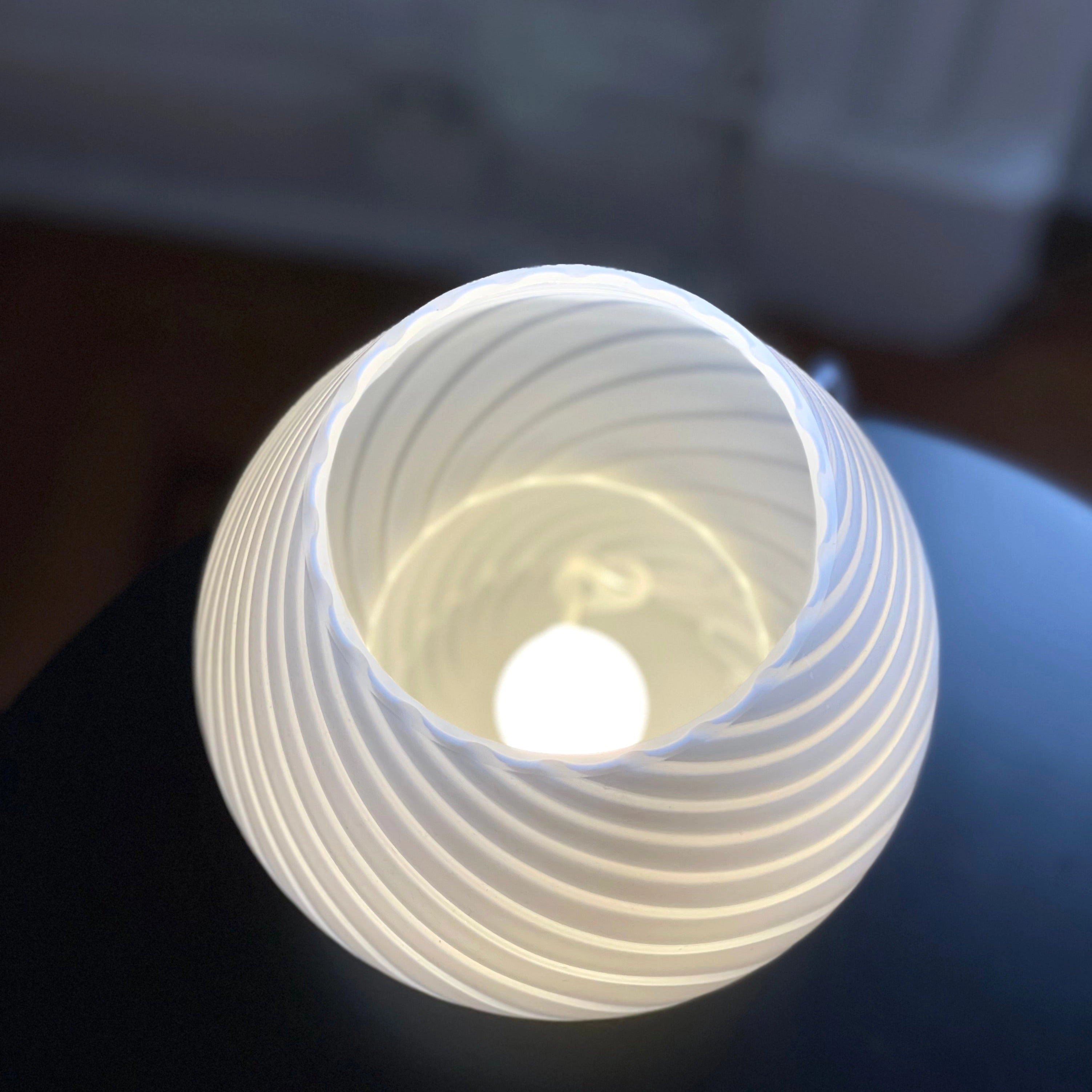 Modern 3D printed white swirl LED table lamp with a cylindrical design, featuring intricate swirling patterns, glowing softly in the darkness.