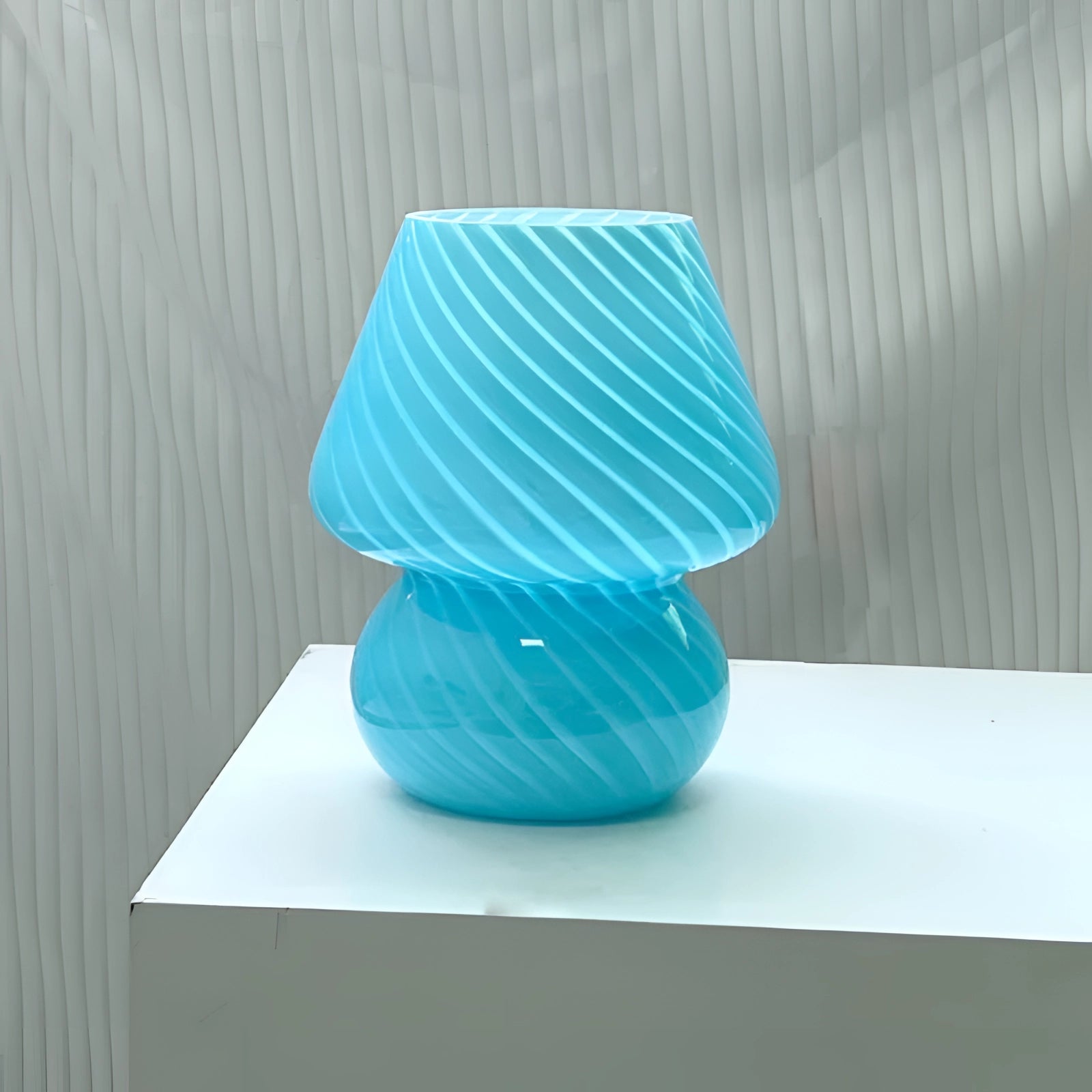 Modern 3D printed table lamp with a blue swirl design, featuring an energy-efficient LED light. The lamp is styled in a vase-like shape and placed on a wooden rectangular table, accompanied by artful decor creating an aesthetically pleasing setting.