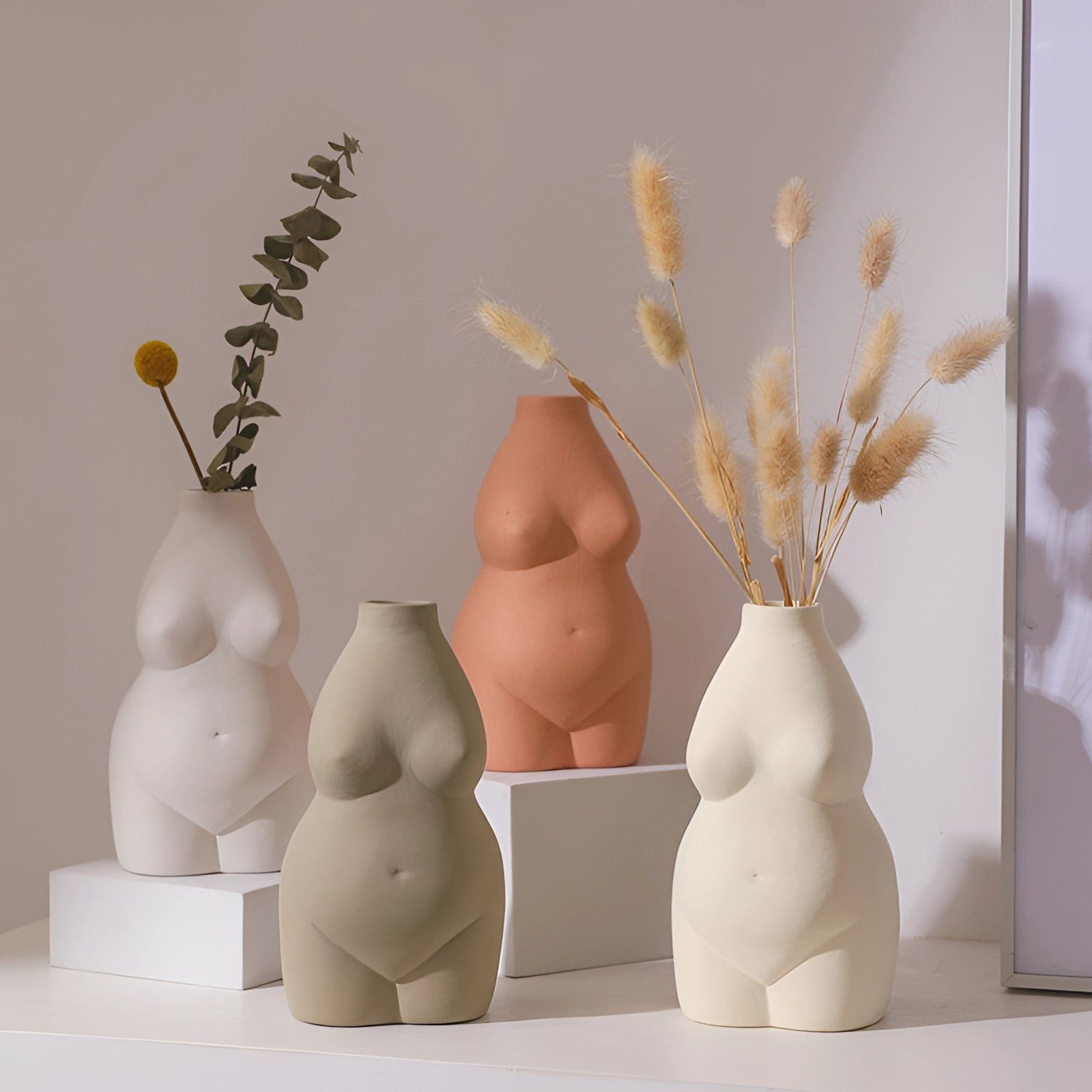 Modern abstract female form vases in an art deco body-shaped design, featuring twig elements and made from natural materials, creatively displayed in a room setting.