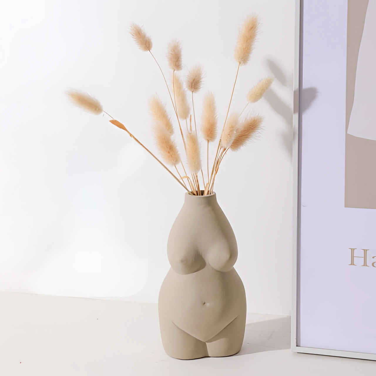 Modern abstract gray vase with a female body-shaped design, displaying an art deco style. The vase is positioned on a wooden surface and is partially filled with twigs, showcasing its artistic and creative appeal.